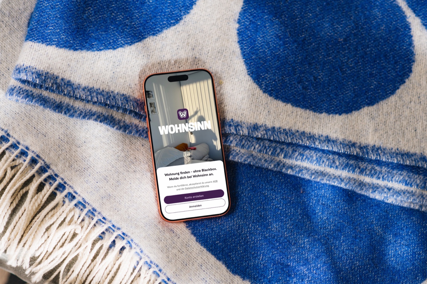 Wohnsinn App auf einem Smartphone vor blau gemustertem Stoff