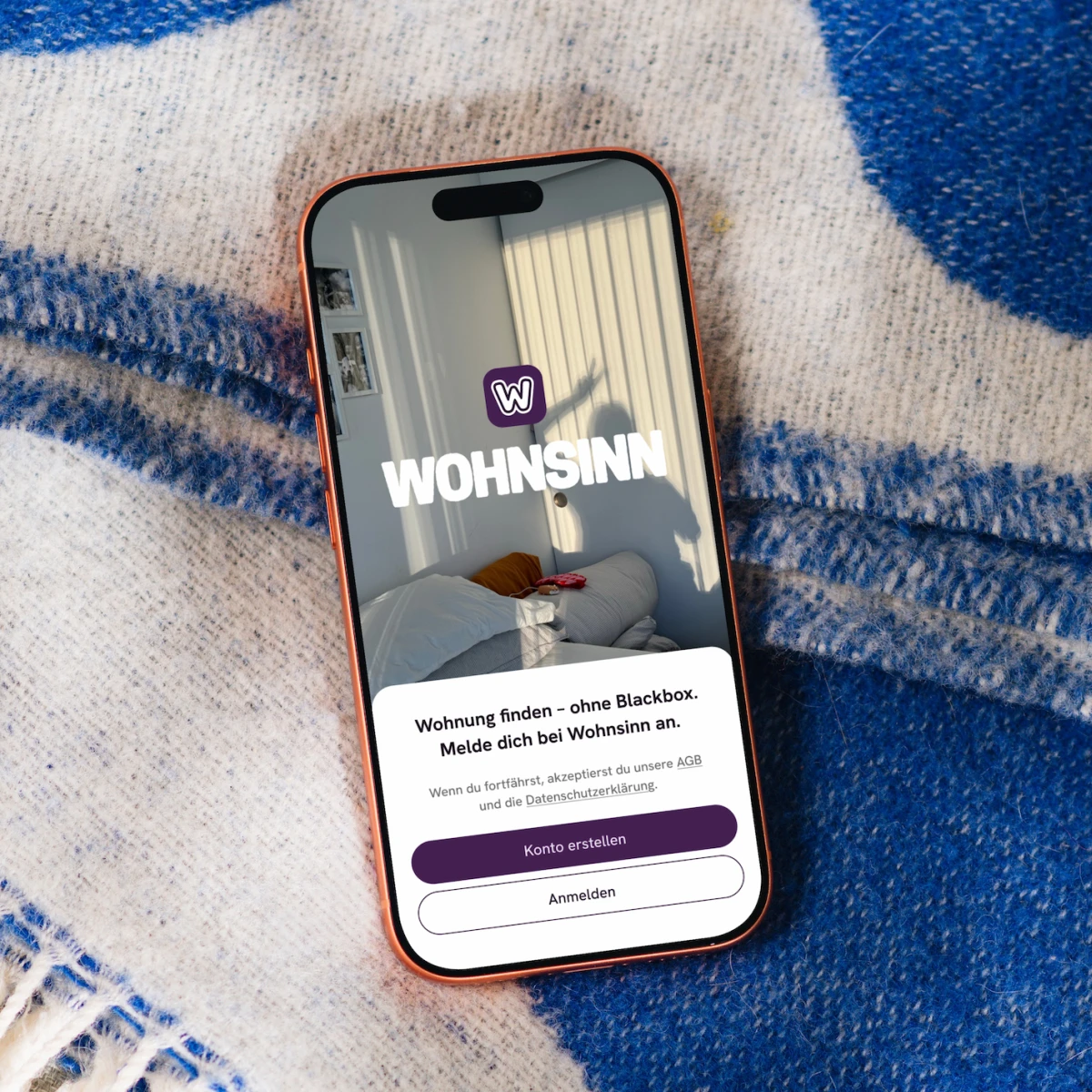 Wohnsinn App auf einem Smartphone vor blau gemustertem Stoff